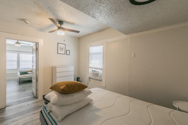 bedroom featuring cooling unit, a textured ceiling, light wood-type flooring, and a ceiling fan