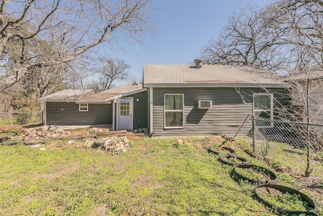 rear view of property featuring a yard, a wall mounted air conditioner, roof with shingles, and fence