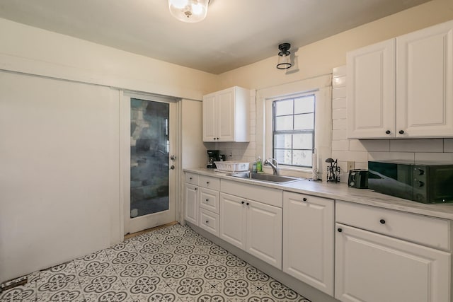 kitchen with a sink, white cabinets, black microwave, light countertops, and decorative backsplash