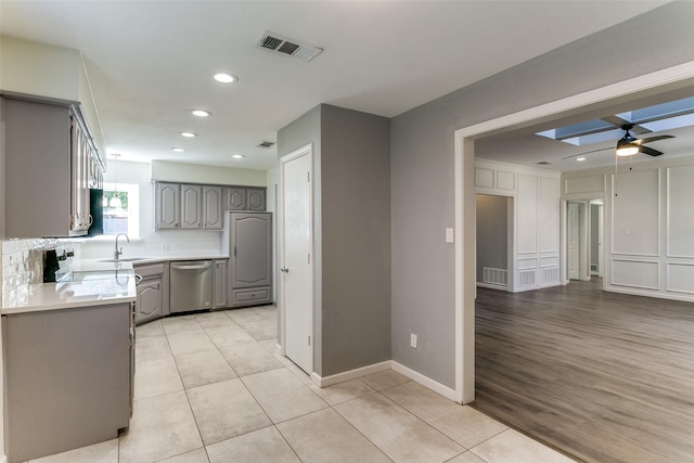 kitchen with visible vents, stainless steel dishwasher, gray cabinets, and a decorative wall