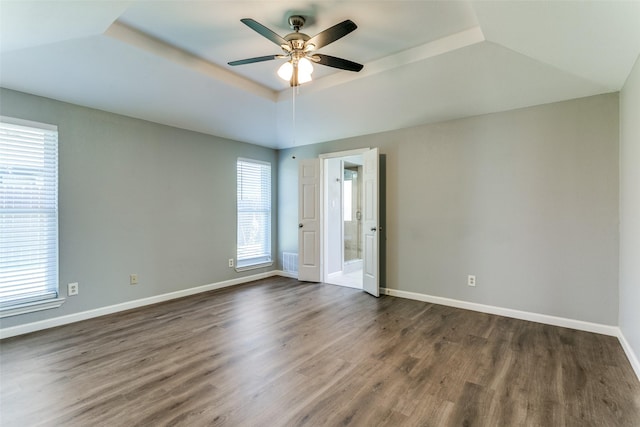 unfurnished room with visible vents, dark wood-type flooring, a ceiling fan, a tray ceiling, and baseboards