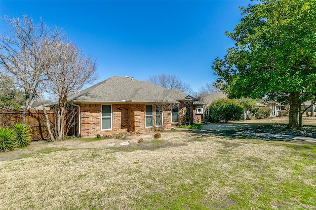 view of front of house with brick siding, roof with shingles, a front lawn, and fence