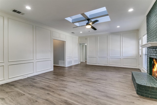 unfurnished living room featuring a brick fireplace, a decorative wall, a skylight, and visible vents