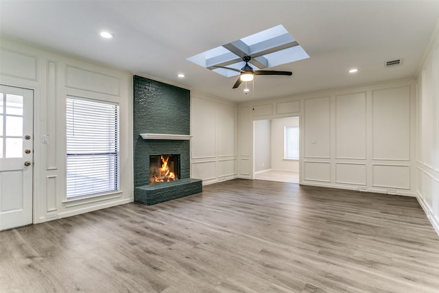 unfurnished living room featuring wood finished floors, a skylight, ornamental molding, a decorative wall, and a large fireplace