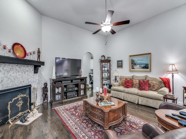 living room with wood finished floors, baseboards, a fireplace, arched walkways, and ceiling fan
