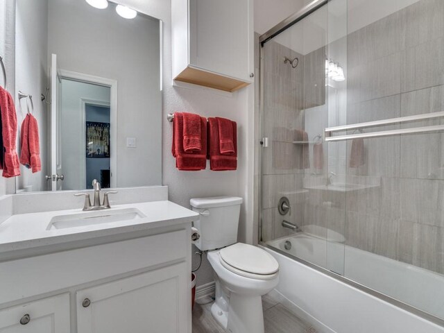full bath featuring toilet, vanity, and shower / bath combination with glass door