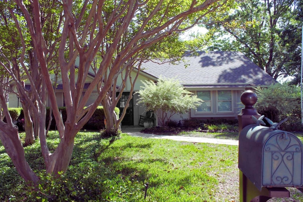 view of property hidden behind natural elements with a shingled roof and a front lawn