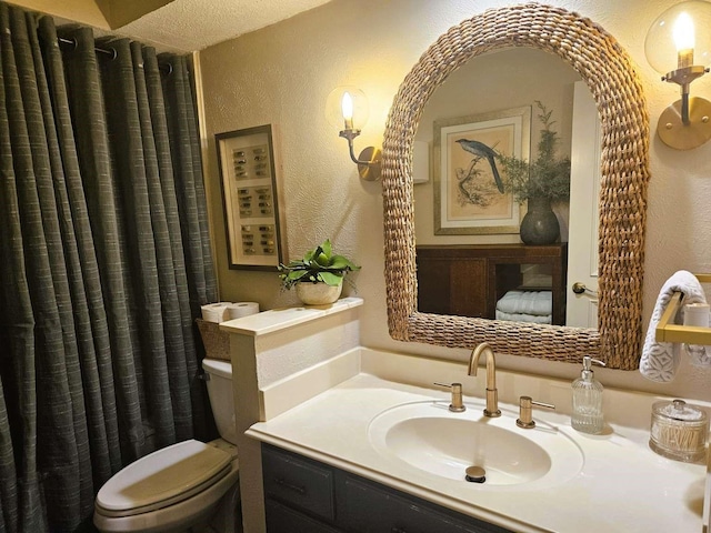 full bath with toilet, vanity, and a textured wall