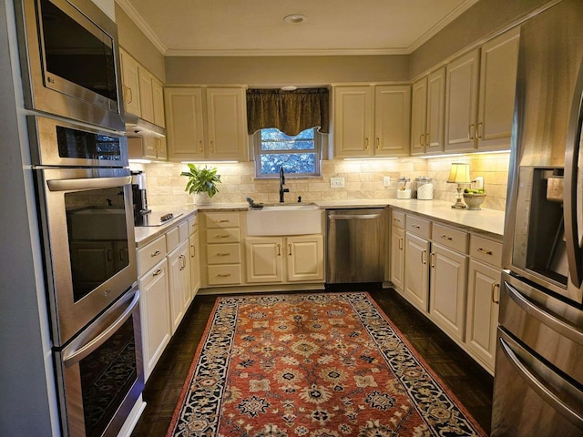 kitchen featuring a sink, light countertops, under cabinet range hood, appliances with stainless steel finishes, and crown molding