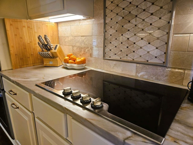 kitchen with tasteful backsplash, white cabinets, light countertops, and black electric cooktop