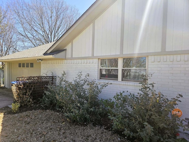 view of side of property featuring brick siding, an attached garage, and a shingled roof