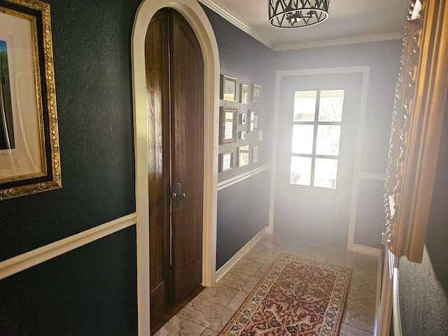 entryway featuring baseboards, arched walkways, ornamental molding, and a textured wall