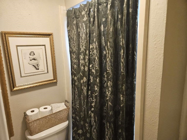 full bathroom featuring a shower with shower curtain, toilet, and a textured wall