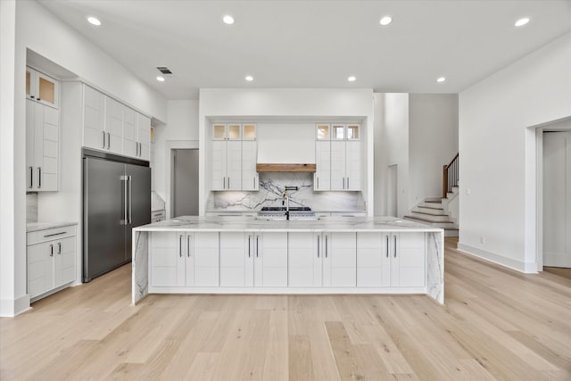 kitchen featuring light wood-type flooring, premium range hood, backsplash, built in fridge, and white cabinetry