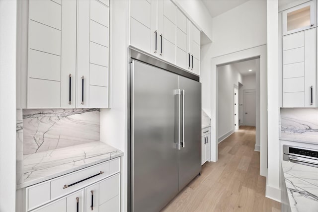 kitchen with backsplash, white cabinets, light stone counters, and built in fridge