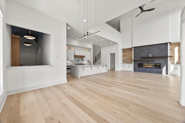 unfurnished living room featuring a sink, light wood-type flooring, a high ceiling, and a fireplace