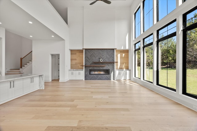 unfurnished living room featuring light wood-style flooring, stairway, a towering ceiling, and a fireplace