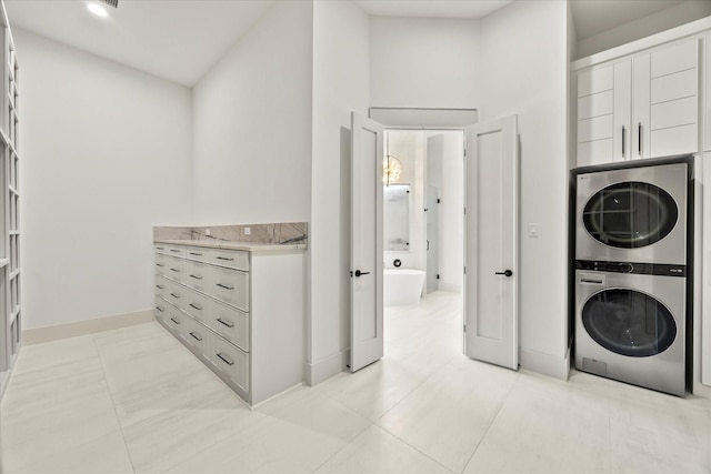 laundry area with light tile patterned floors, baseboards, stacked washer and clothes dryer, and laundry area