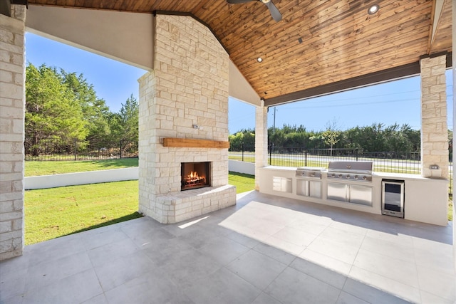 view of patio featuring a grill, a ceiling fan, fence, an outdoor stone fireplace, and an outdoor kitchen