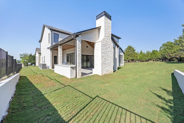 rear view of property with a chimney, stone siding, a patio area, fence, and a lawn