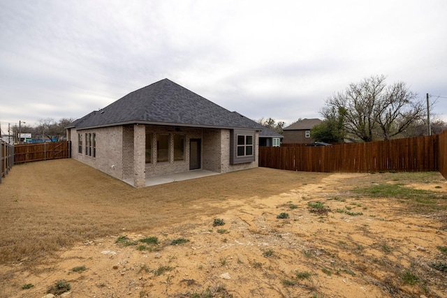 rear view of house with a patio area, a fenced backyard, brick siding, and roof with shingles
