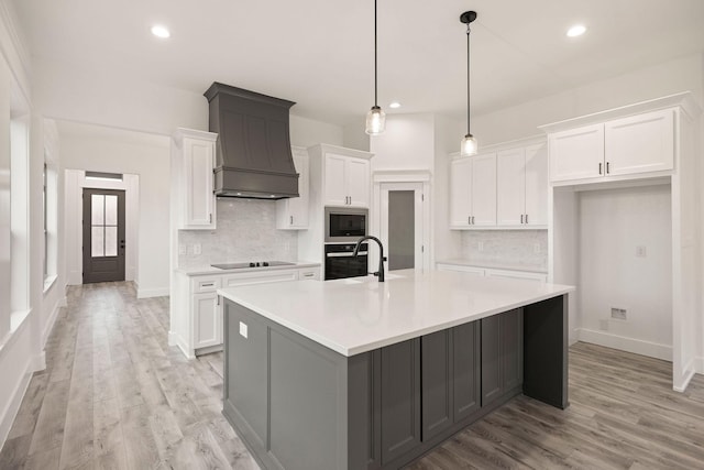 kitchen with premium range hood, a large island with sink, black appliances, white cabinets, and light countertops