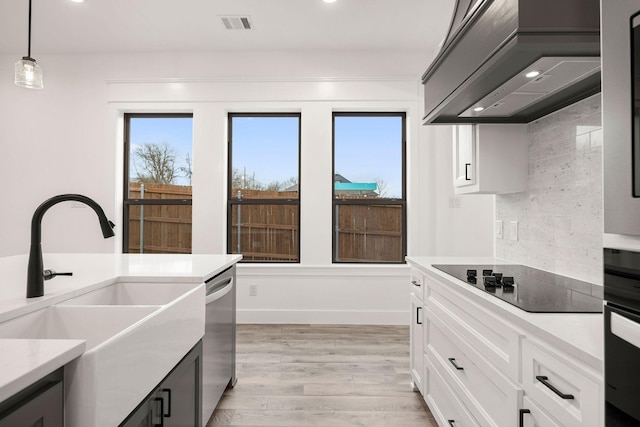 kitchen featuring a sink, light wood-style floors, black electric stovetop, custom exhaust hood, and dishwasher
