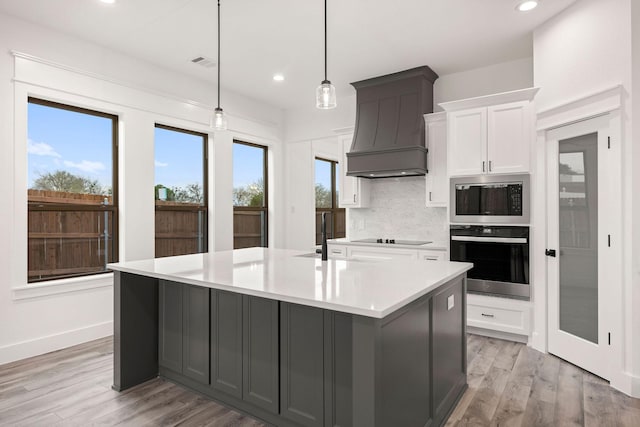 kitchen featuring custom exhaust hood, built in microwave, decorative backsplash, a large island, and stainless steel oven