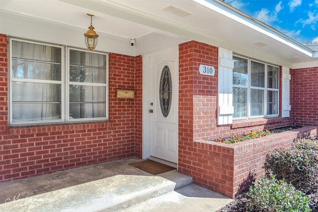 property entrance featuring brick siding and visible vents