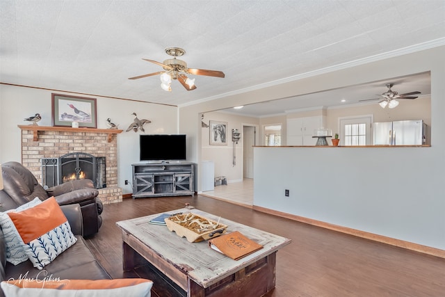 living room with wood finished floors, baseboards, ceiling fan, crown molding, and a brick fireplace