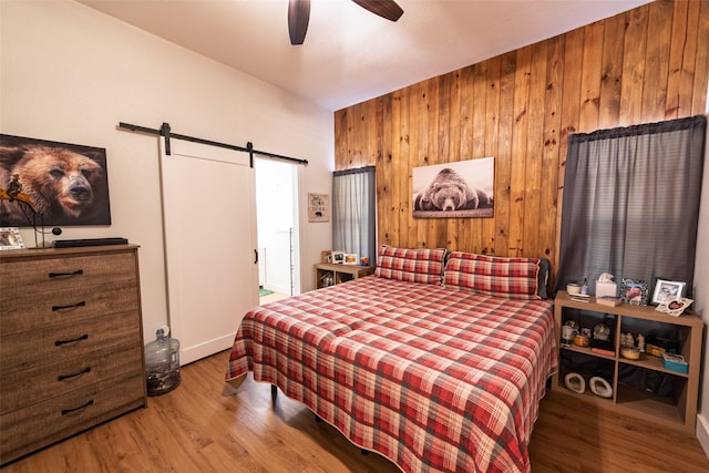 bedroom featuring wood walls, a ceiling fan, a barn door, and wood finished floors