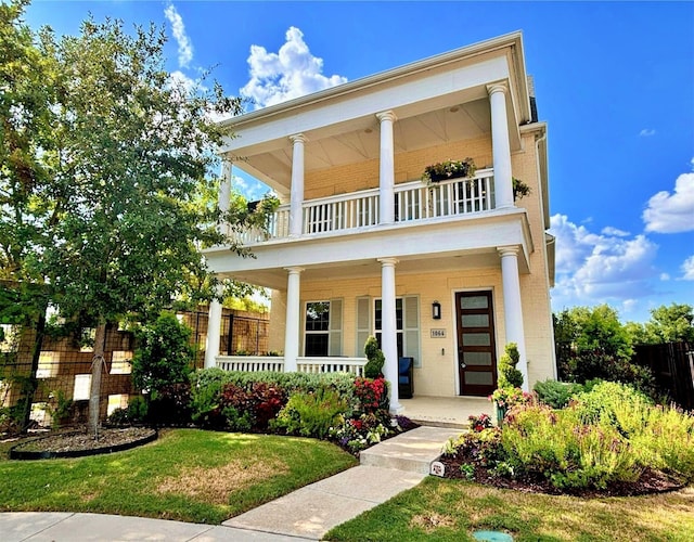 neoclassical home with a balcony, covered porch, a front yard, and fence