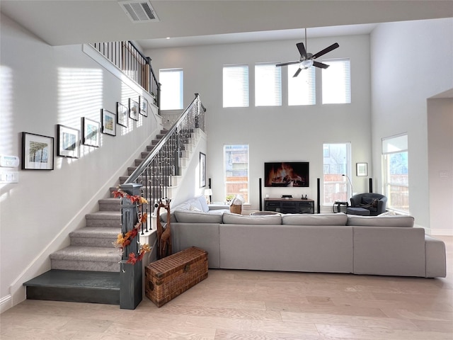 living area featuring stairway, baseboards, visible vents, a high ceiling, and ceiling fan