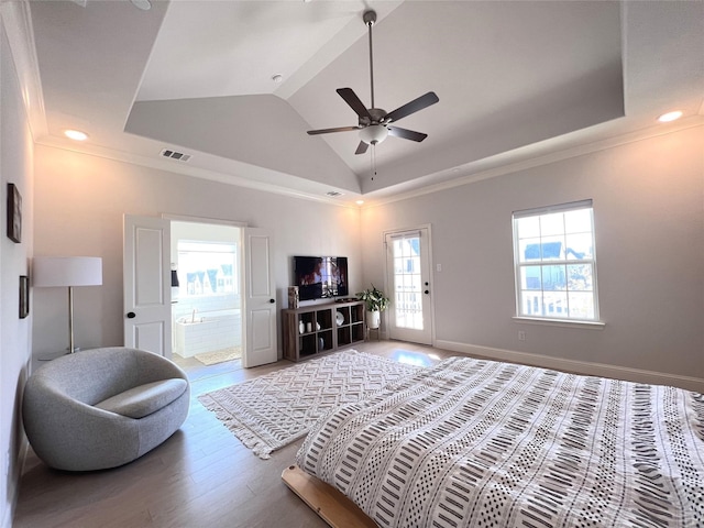 bedroom with a tray ceiling, wood finished floors, visible vents, and baseboards