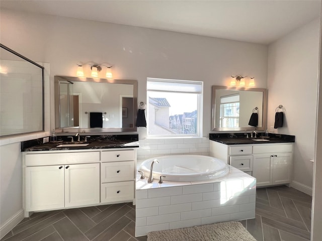 full bathroom featuring two vanities, a bath, baseboards, and a sink