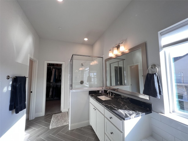 bathroom with a walk in closet, a stall shower, recessed lighting, baseboards, and vanity