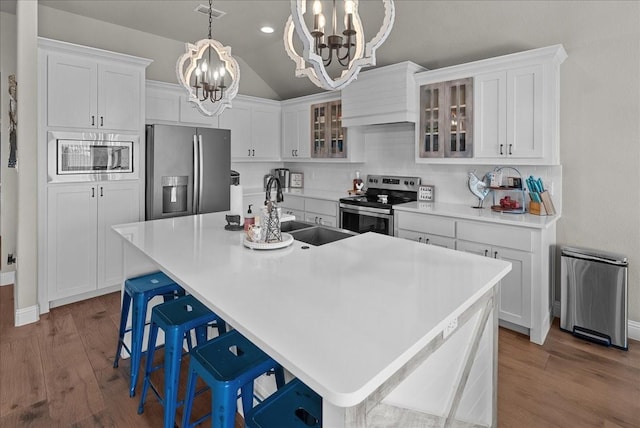 kitchen with a chandelier, wood finished floors, appliances with stainless steel finishes, and a center island with sink