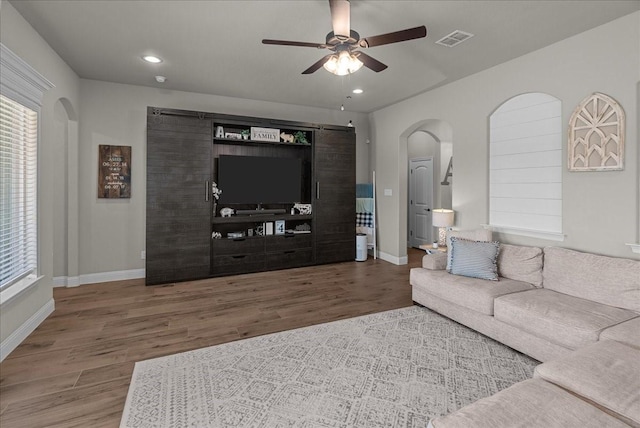 living area featuring arched walkways, a ceiling fan, wood finished floors, and baseboards