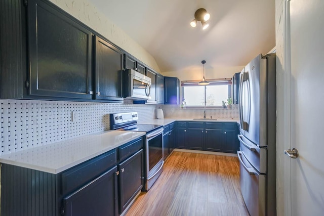 kitchen with backsplash, light countertops, lofted ceiling, light wood-style floors, and stainless steel appliances