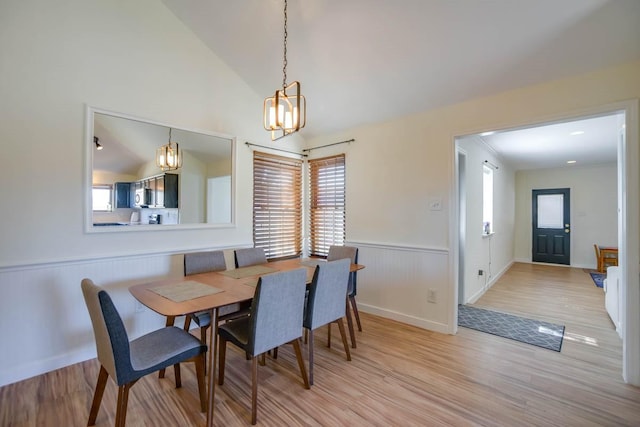 dining room with a wainscoted wall, light wood-type flooring, lofted ceiling, and an inviting chandelier