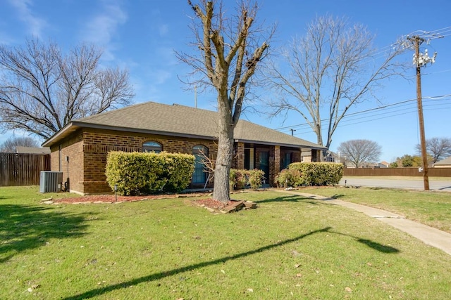 view of front facade with fence, cooling unit, roof with shingles, a front yard, and brick siding