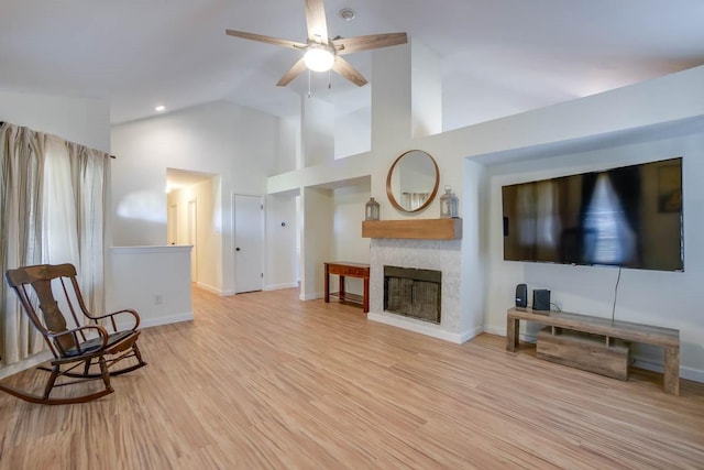 living area featuring baseboards, high vaulted ceiling, a fireplace, ceiling fan, and light wood-style floors