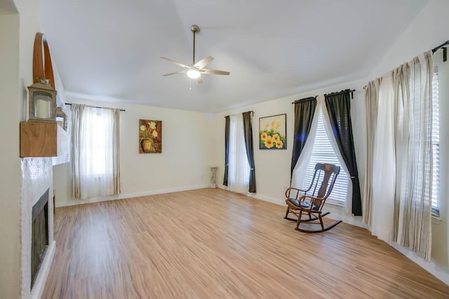 unfurnished room featuring a ceiling fan, baseboards, light wood finished floors, a fireplace, and vaulted ceiling