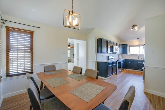 dining area featuring a wainscoted wall, a notable chandelier, vaulted ceiling, and light wood finished floors