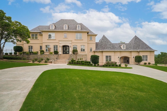 french country home featuring stucco siding, curved driveway, and a front yard