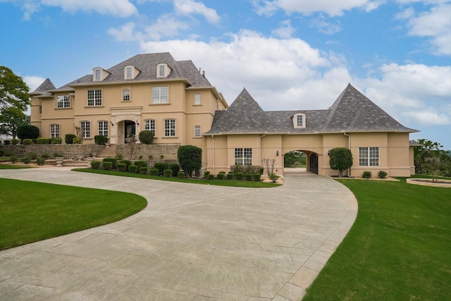 french provincial home featuring stucco siding, curved driveway, and a front yard