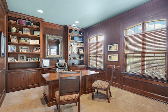 office area with wooden walls, light colored carpet, built in shelves, and visible vents