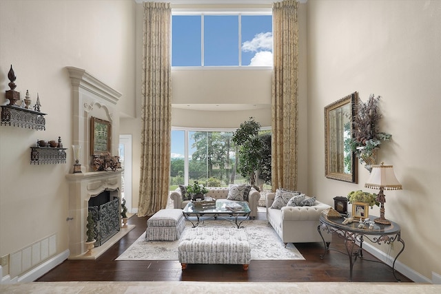 living room with visible vents, a fireplace with raised hearth, hardwood / wood-style floors, baseboards, and a towering ceiling