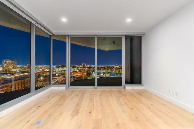 empty room with a view of city lights, baseboards, wood finished floors, recessed lighting, and expansive windows