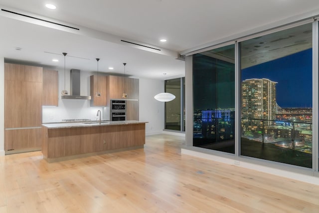 kitchen with wall chimney range hood, a sink, modern cabinets, and light wood-type flooring